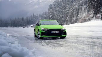 Hellgrüner Audi RS 3 Sportback auf vereister Fläche vor verschneitem Wald und Bergen bei winterlichem Wetter.