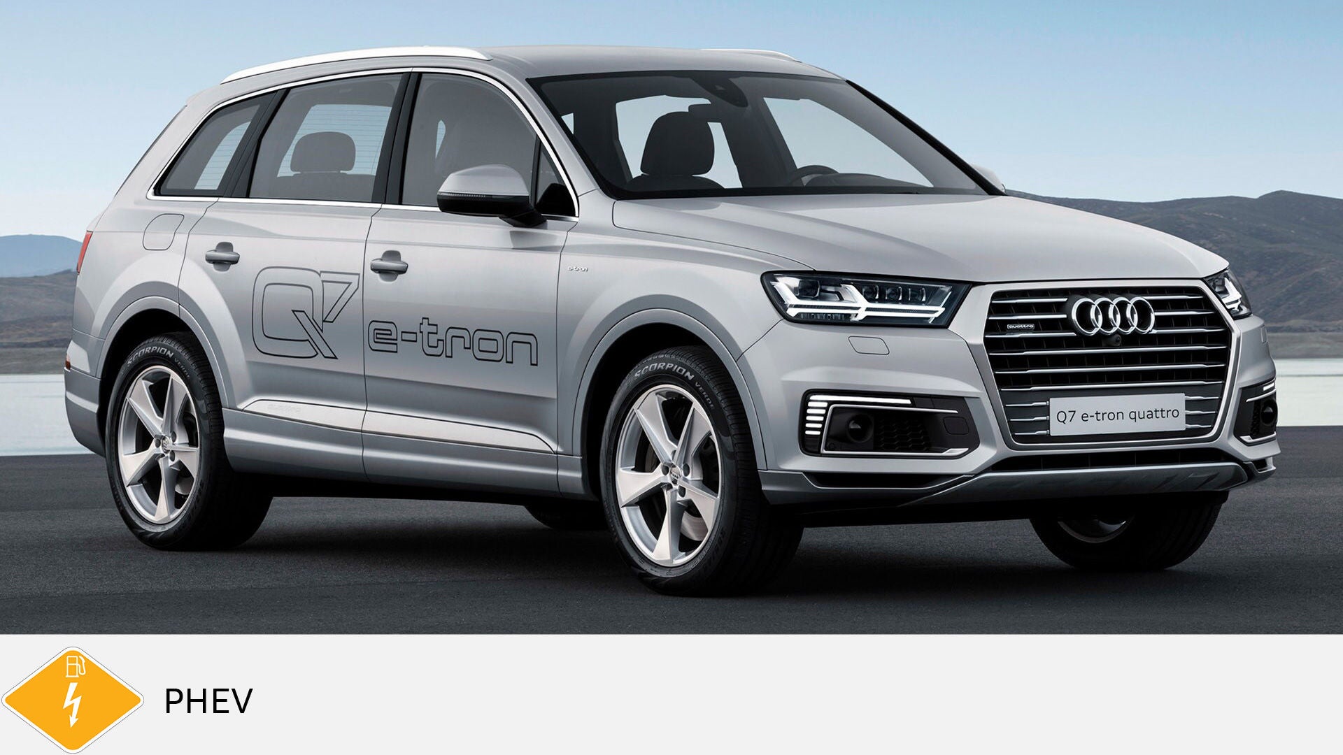 Silver Audi Q7 e-tron quattro with large e-tron lettering stands by the water. Yellow PHEV symbol with petrol pump below.