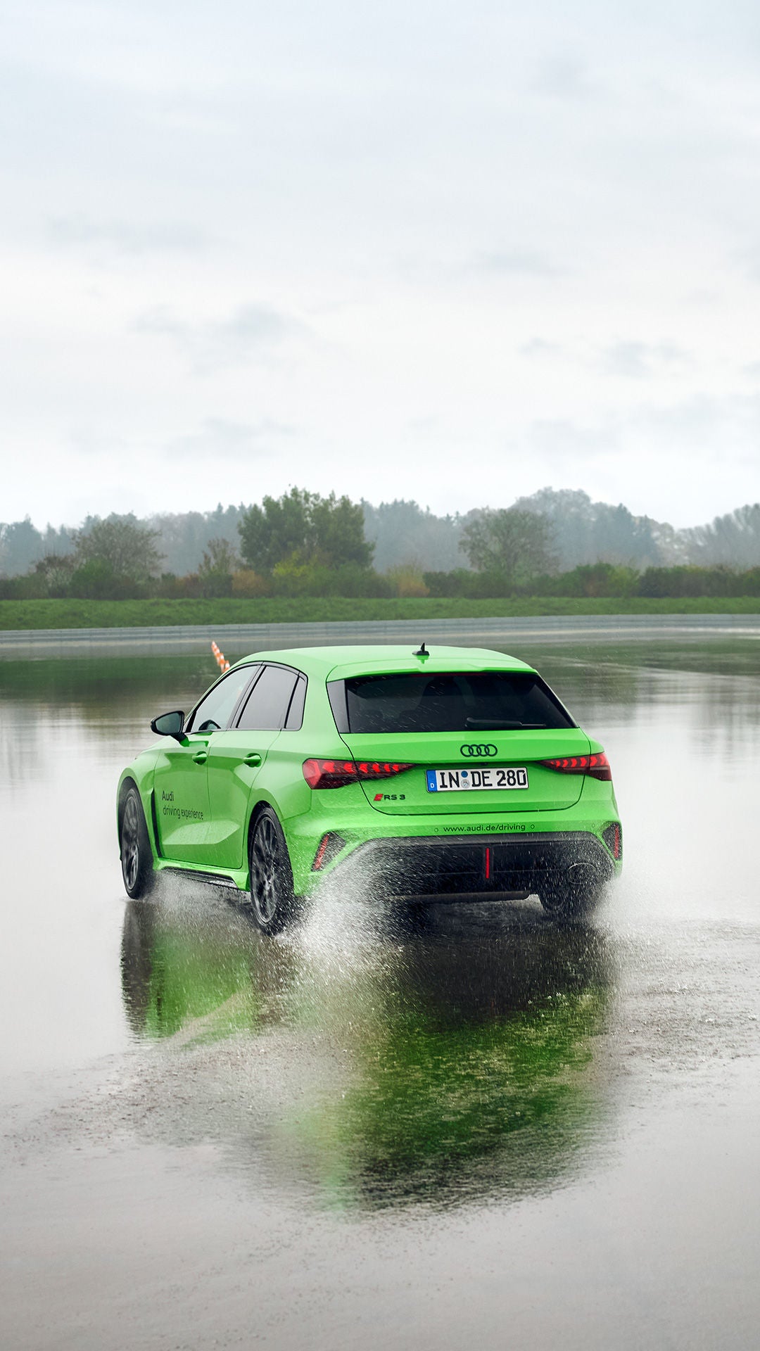 Hellgrüner Audi RS 3 Sportback fährt auf einem Übungsgelände über eine große Pfütze.