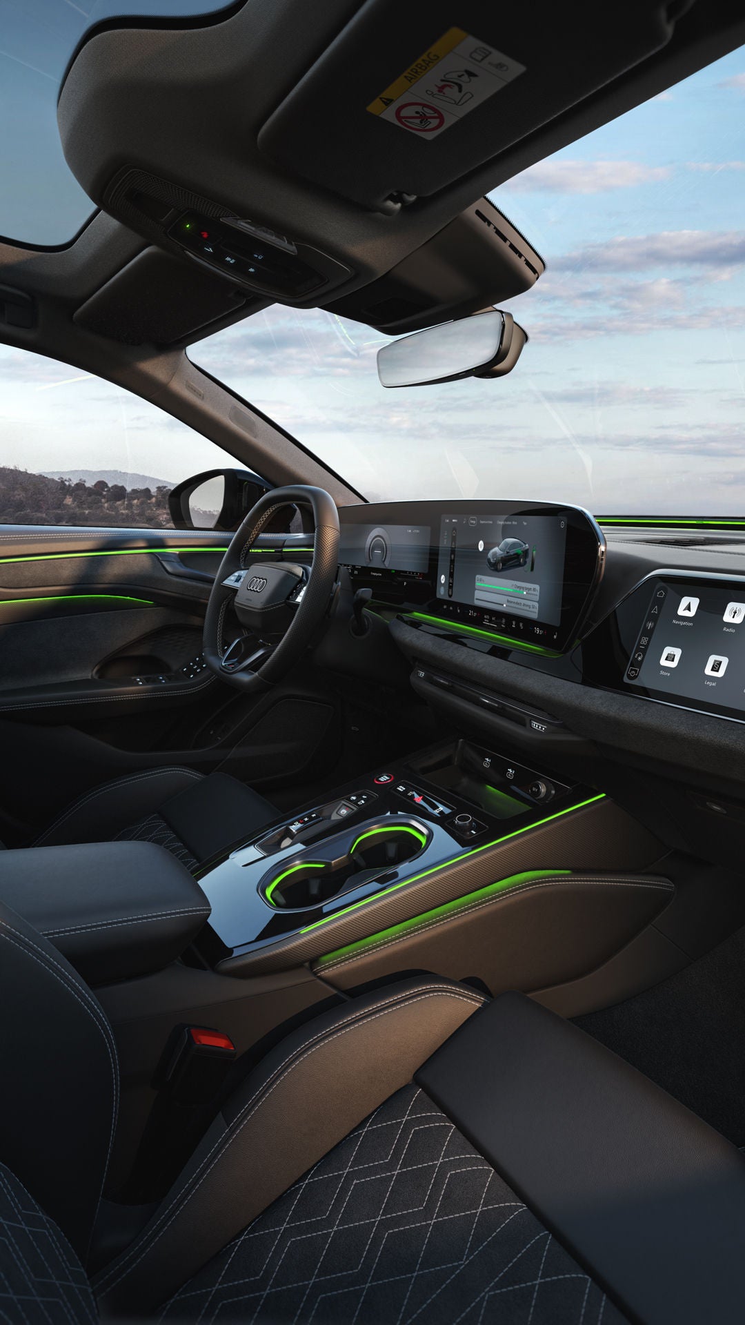 The cockpit of the A6 Saloon e-hybrid viewed from the passenger seat. The focus is on the steering wheel, the panoramic displays, and the green ambient lighting.