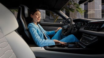 A person wearing a light blue suit sits inside a modern car, interacting with the sleek dashboard and touchscreen displays.