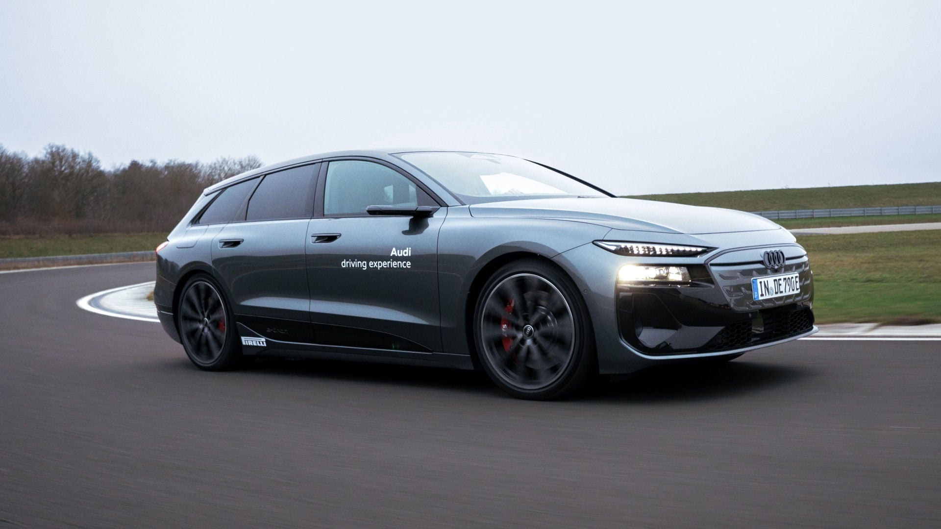 Audi S6 Avant e-tron fährt in eine Kurve auf einer Teststrecke. Im Hintergrund sind Bäume und eine abgegrenzte Grünfläche zu sehen.