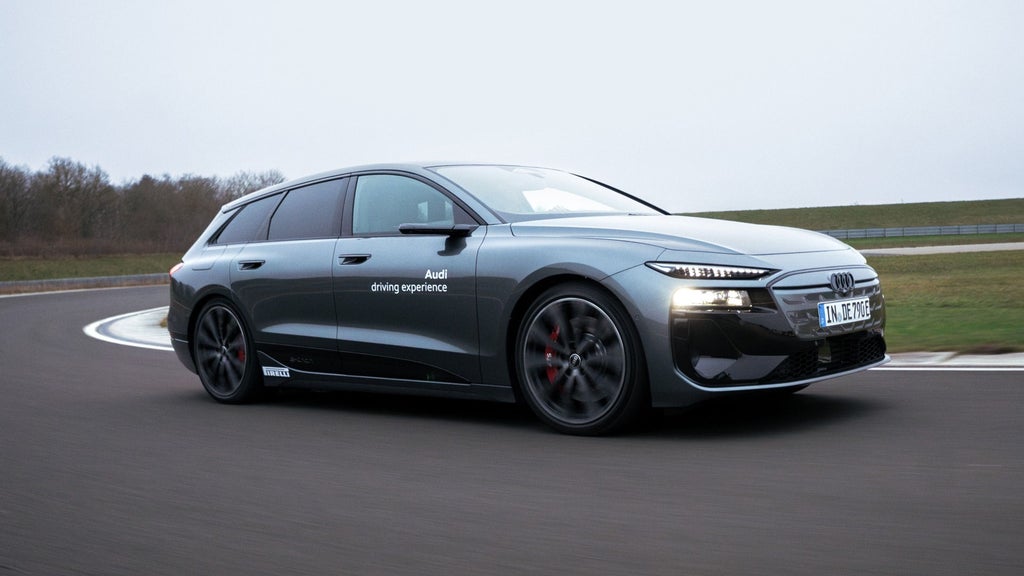 Audi S6 Avant e-tron fährt in eine Kurve auf einer Teststrecke. Im Hintergrund sind Bäume und eine abgegrenzte Grünfläche zu sehen. 