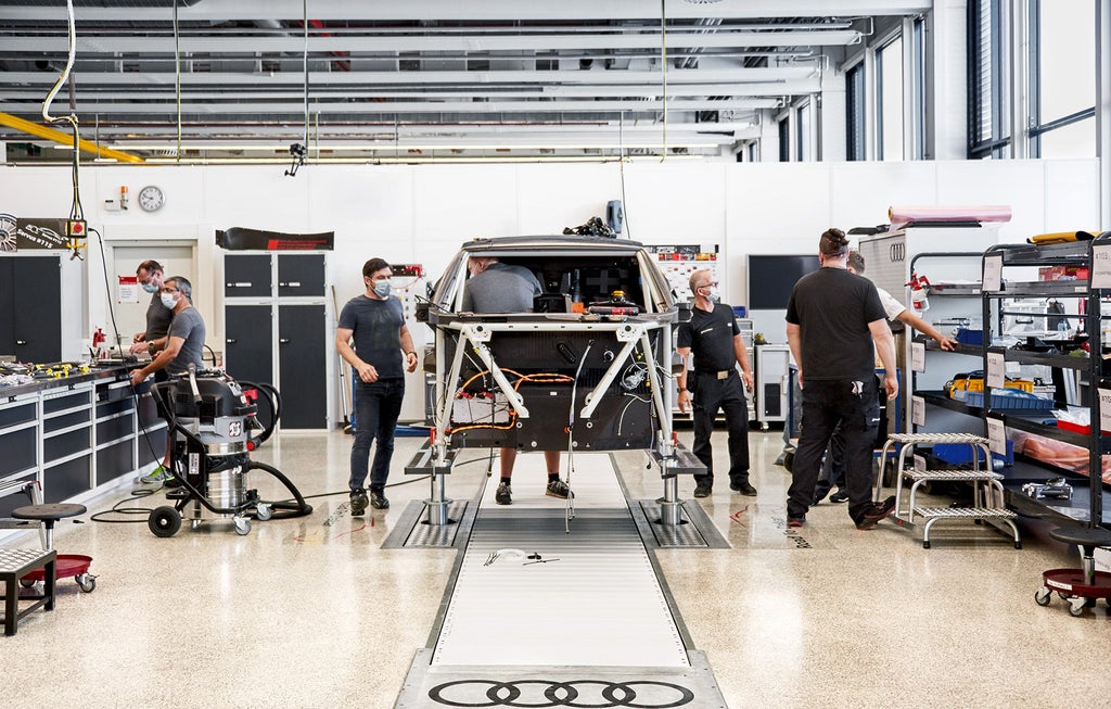 Audi Sport employees work on the rally car’s elevated cage in a workshop.