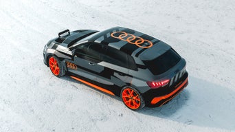 Schwarz-orange foliertes Audi RS 3 Fahrerlebnis mit auffälligem Raddesign steht auf einer schneebedeckten Fläche, fotografiert von schräg oben.