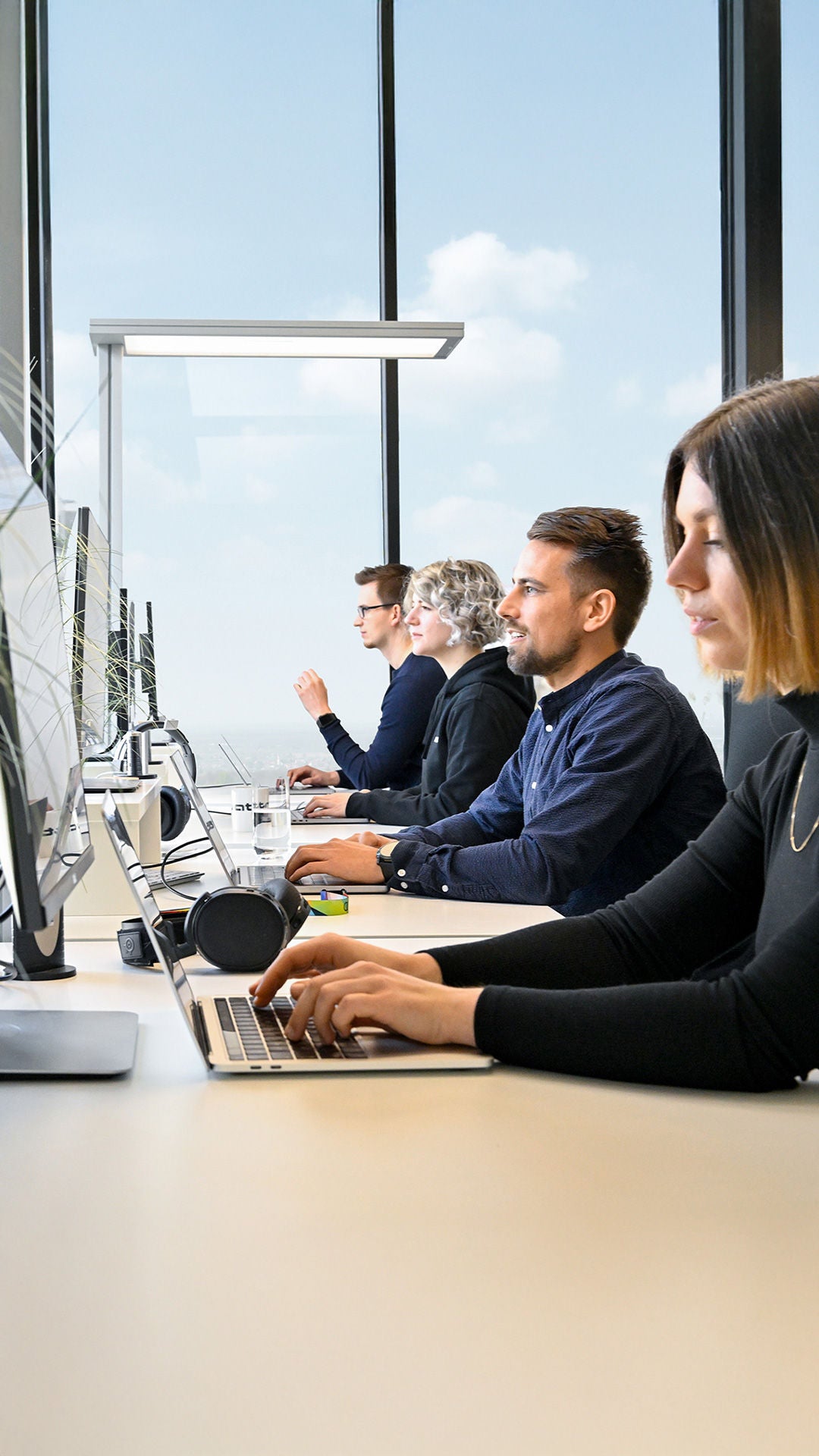 Mitarbeitende des Audi Software Development Center sind an der Arbeit und haben Laptops vor sich