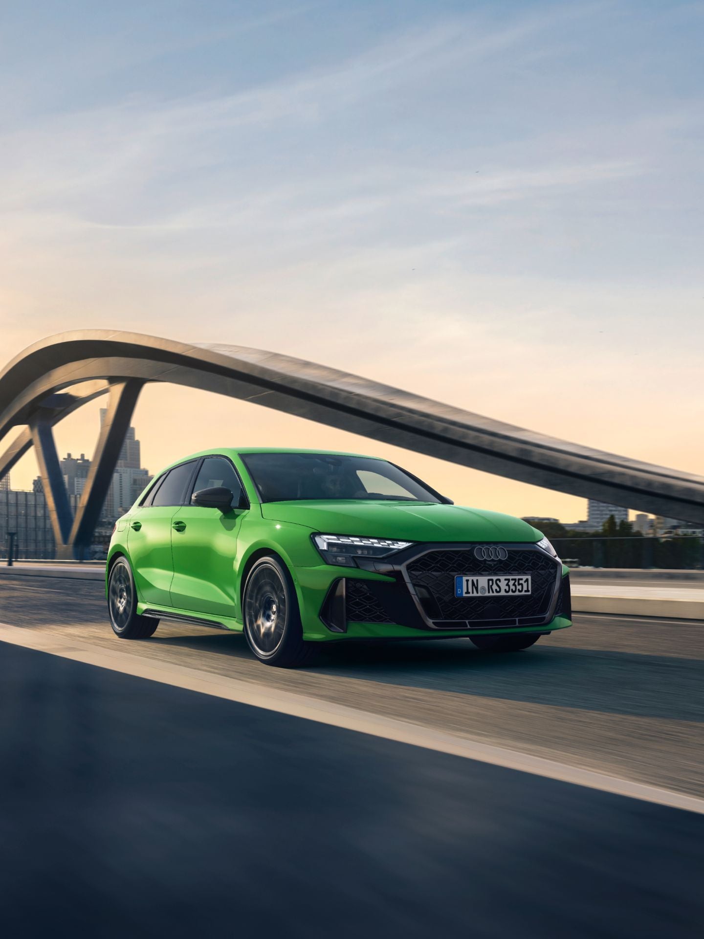 Green Audi RS3 Sportback driving on a bridge with city skyline in the background.