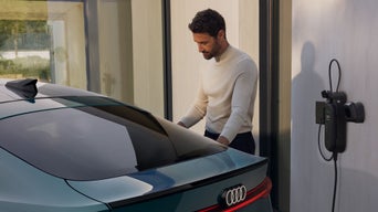 Ein junger Mann steht am Heck des S6 Sportback e-tron und schließt das Fahrzeug an eine Ladestation, die an der Wand montiert ist, an.