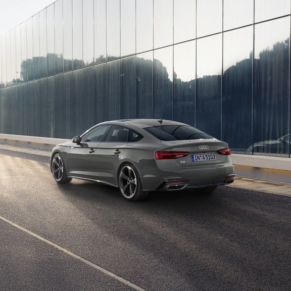 A grey Audi A5 Sportback parked on the roadside with reflective glass buildings in the background.