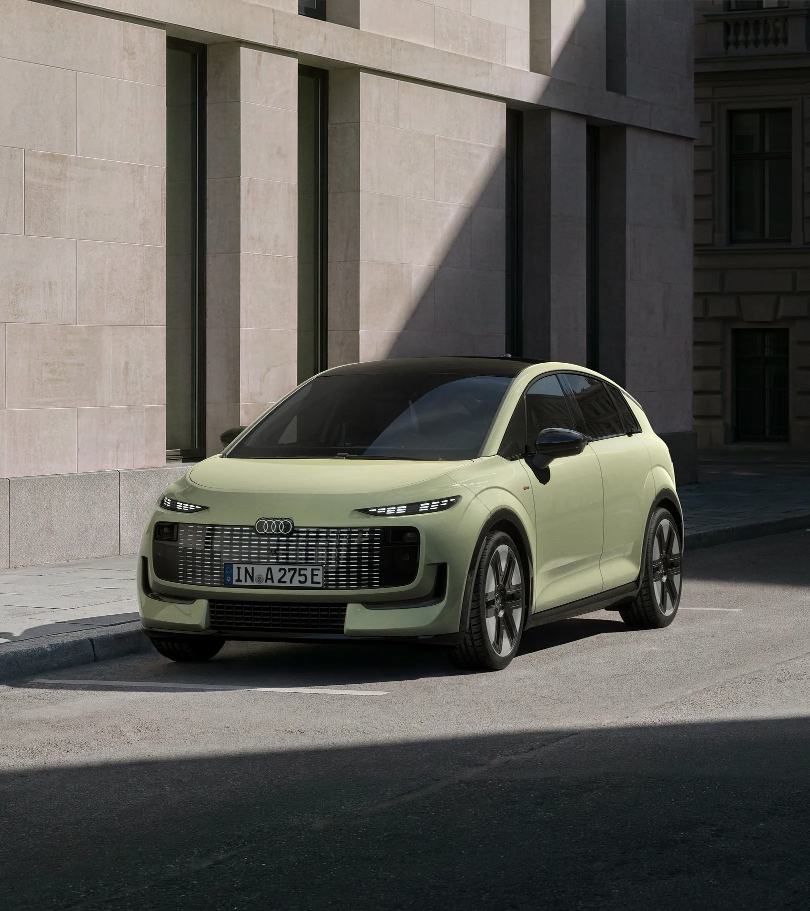 Pistachio green Audi A2 e-tron electric hatchback parked on a city street next to a modern stone building