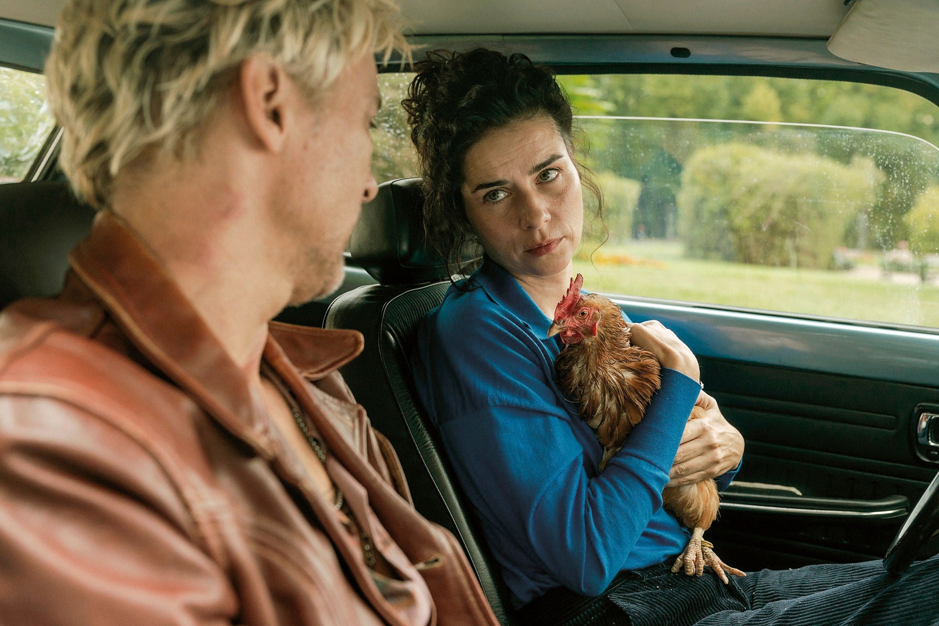 Lissi mit einem Huhn auf dem Arm und Daniel unterhalten sich in einem Auto.