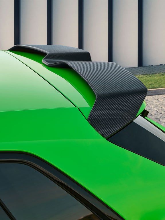 Heckansicht eines Audi RS 3 Sportback mit schwarzem Carbonfaser-Spoiler auf der Kofferraumklappe und leuchtenden Rücklichtern.