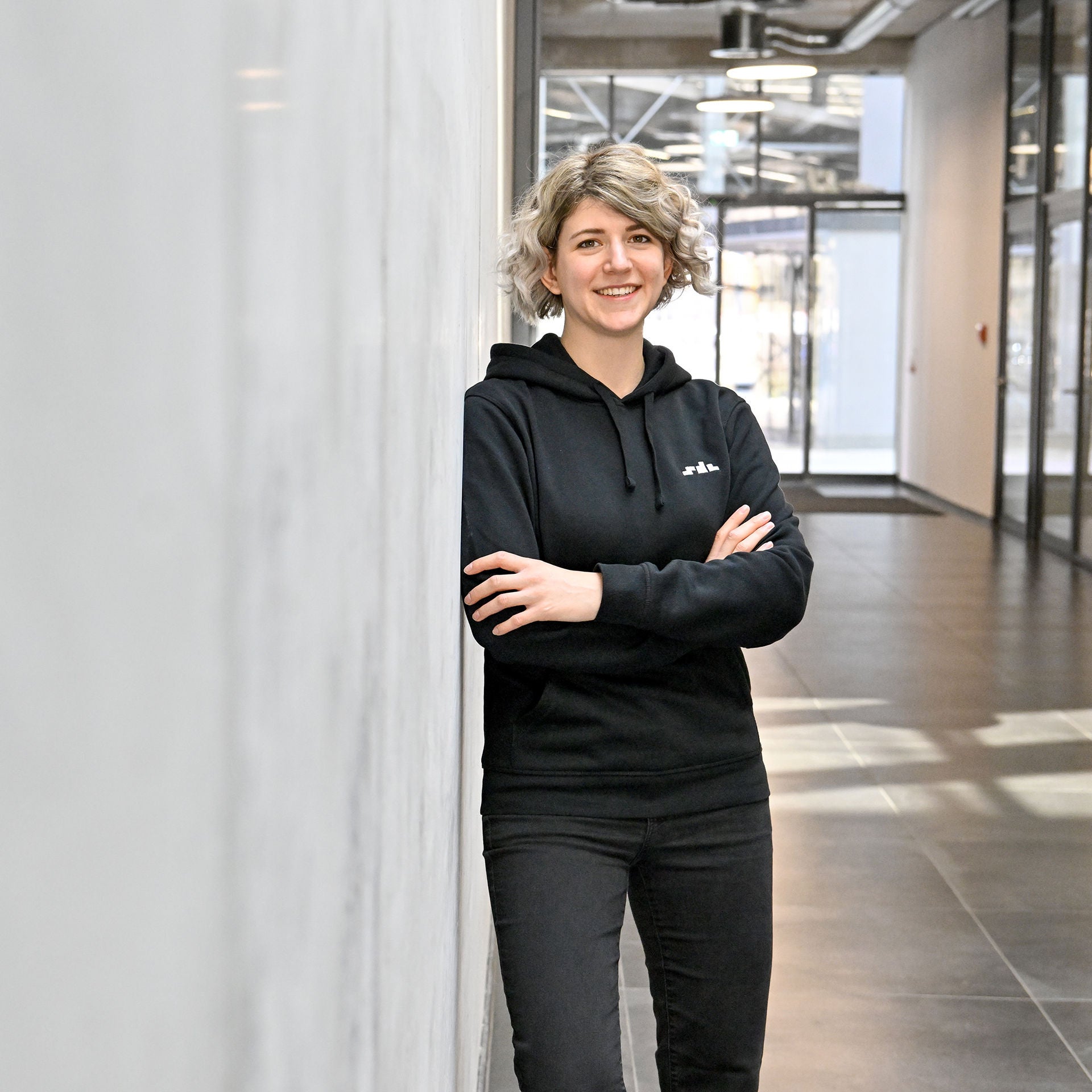 Nadine, Software Engineer SDC, leans against a wall and looks into the camera