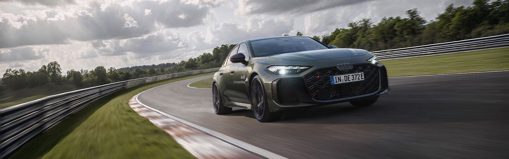 Grüne Audi RS 5 Limousine fährt durch Kurve auf Rennstrecke, bewölkter Himmel im Hintergrund.