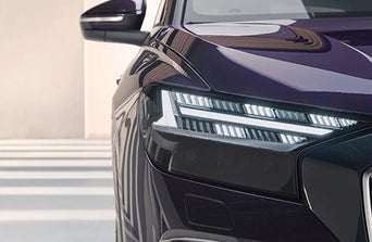 Close-up of a Audi front showcasing its stylish headlight design and glossy purple finish in a minimalistic setting.
