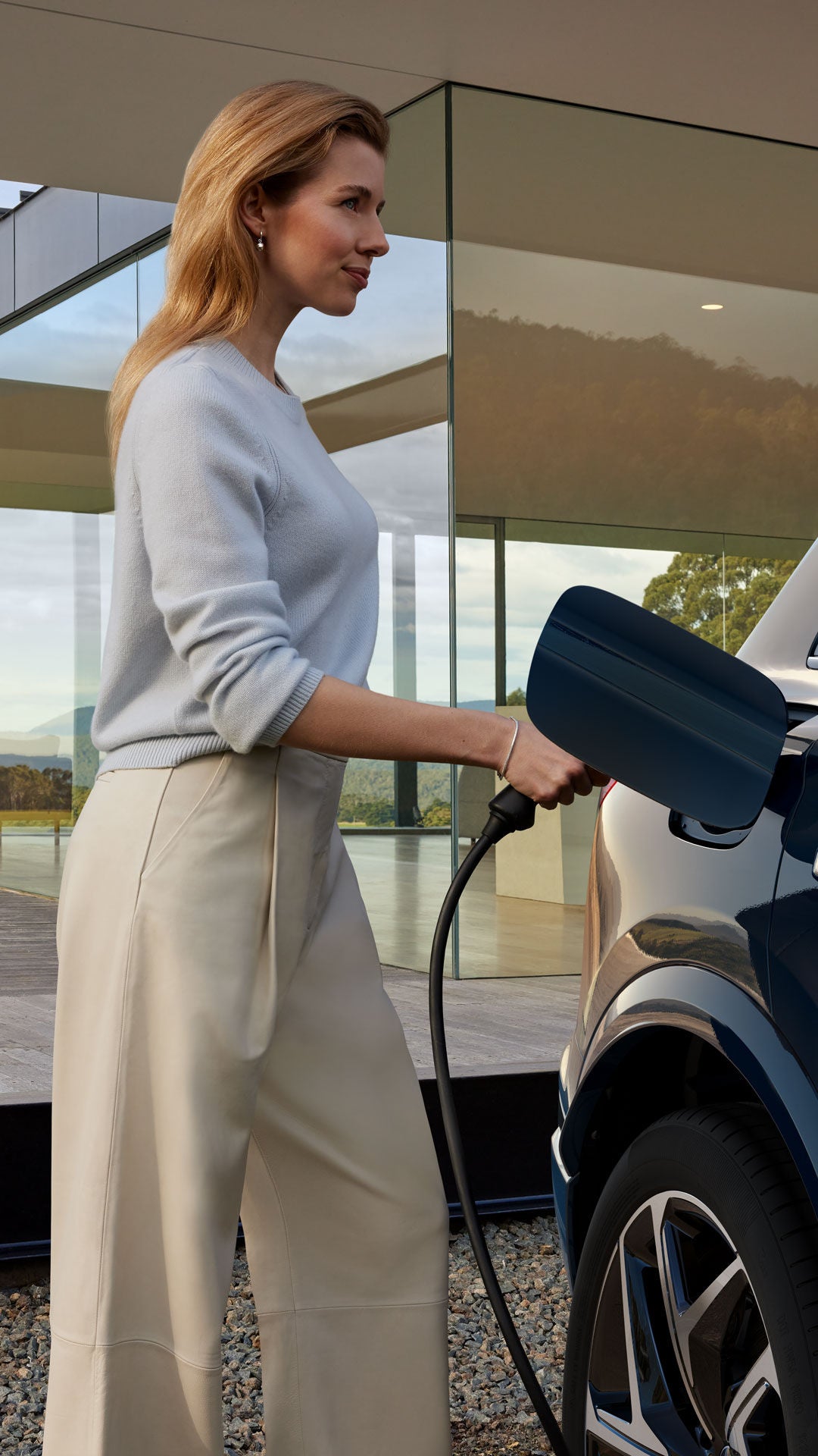 Frau lädt ein Elektroauto an einer modernen Ladesäule vor einem verglasten Gebäude.