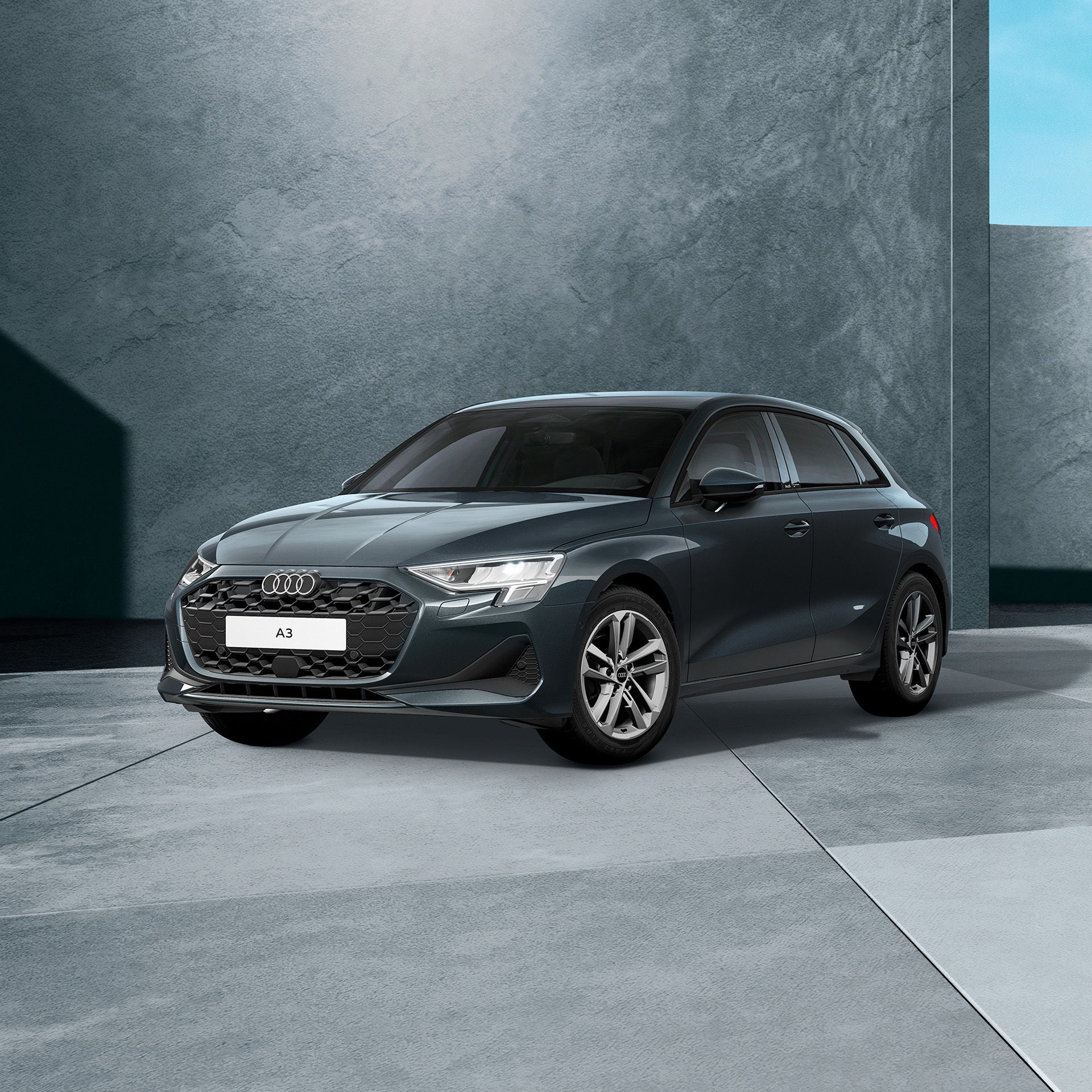 Ein graublauer Audi A3 Sportback von schräg vorne fotografiert vor einer modernen Kulisse.