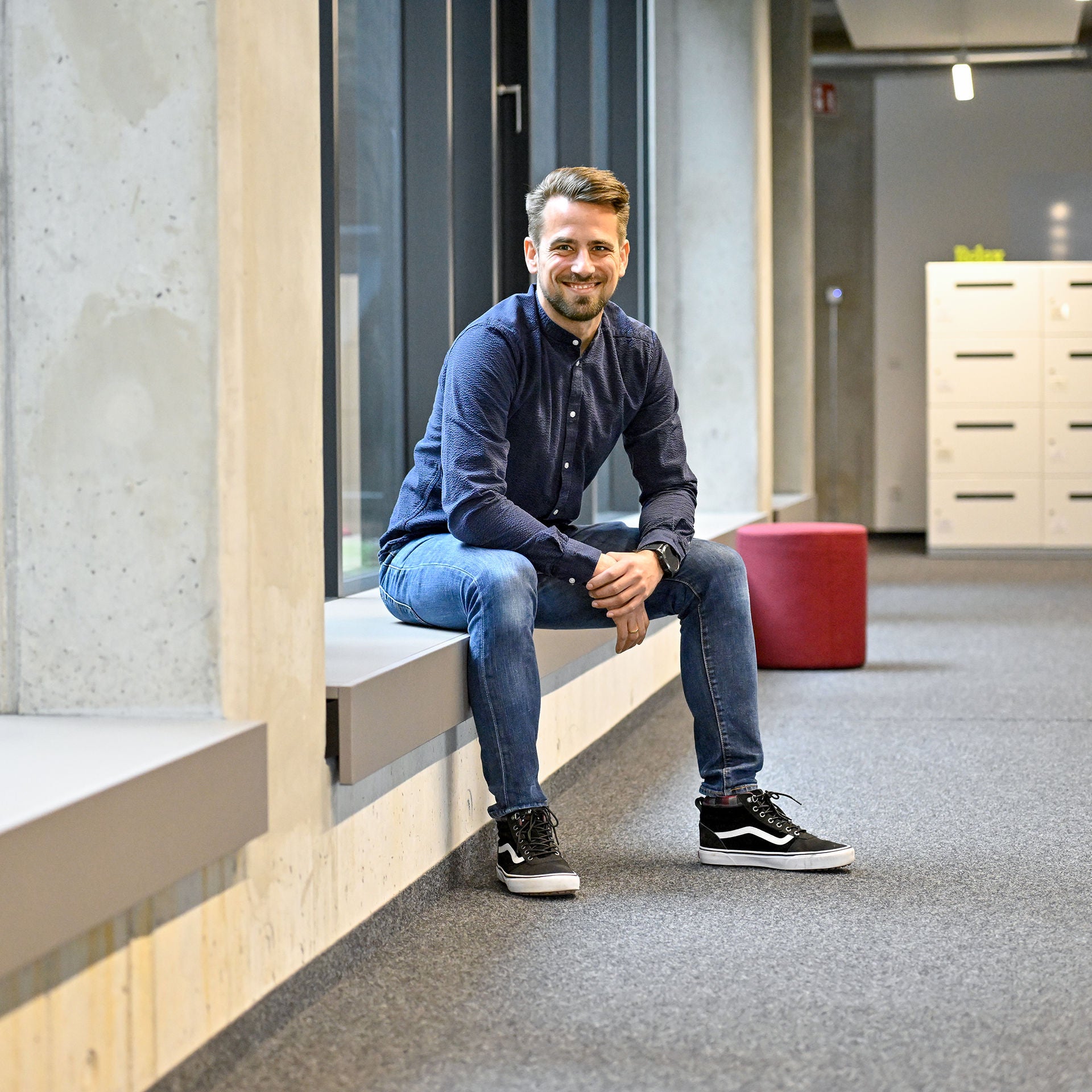 Markus, Product Manager SCD, sitzt auf einer Fensterbank und lacht in die Kamera