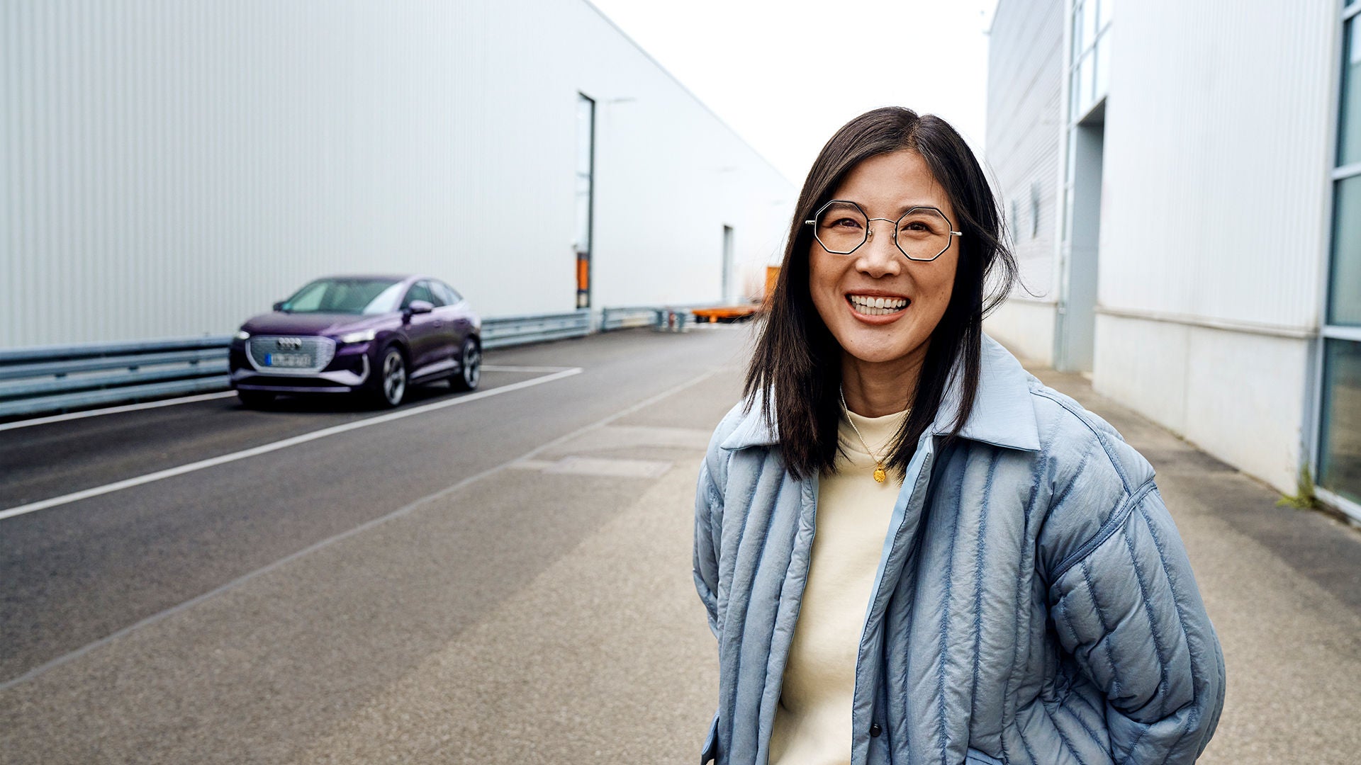 Tiantian steht vor einem lilanen Audi und lächelt in die Kamera.