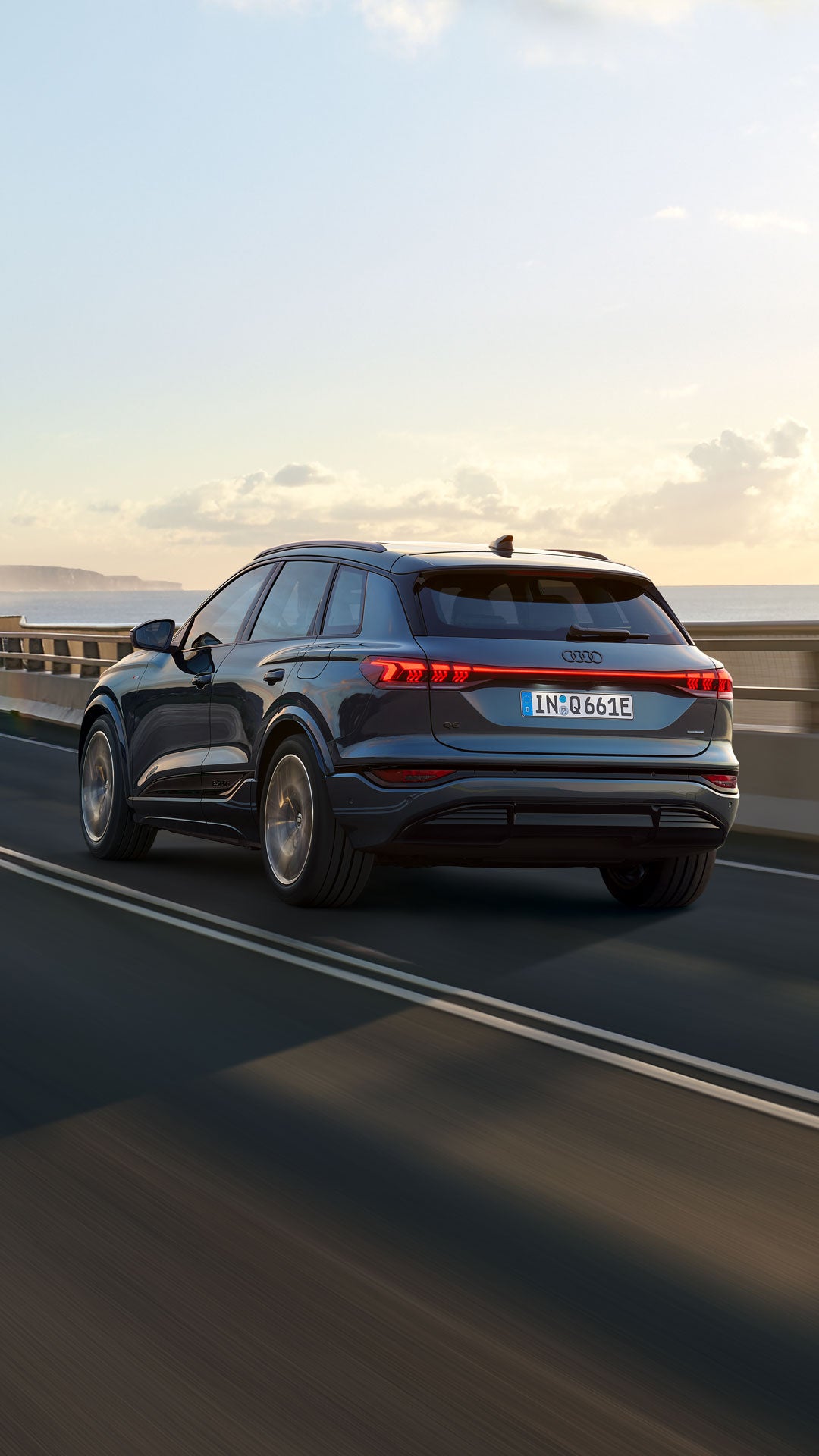 Ein blauer Audi Q6 SUV auf der Straße in ländlichem Setting und Gegenlicht.