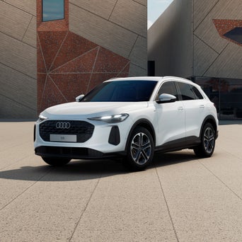 Ein weißer Audi Q5 SUV e-hybrid steht schräg vor einem modernen Gebäude