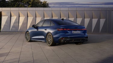 Die S5 Limousine in dunkelblau steht schräg vor einer Gebäudefassade und wird dabei vom Sonnenlicht angestrahlt.