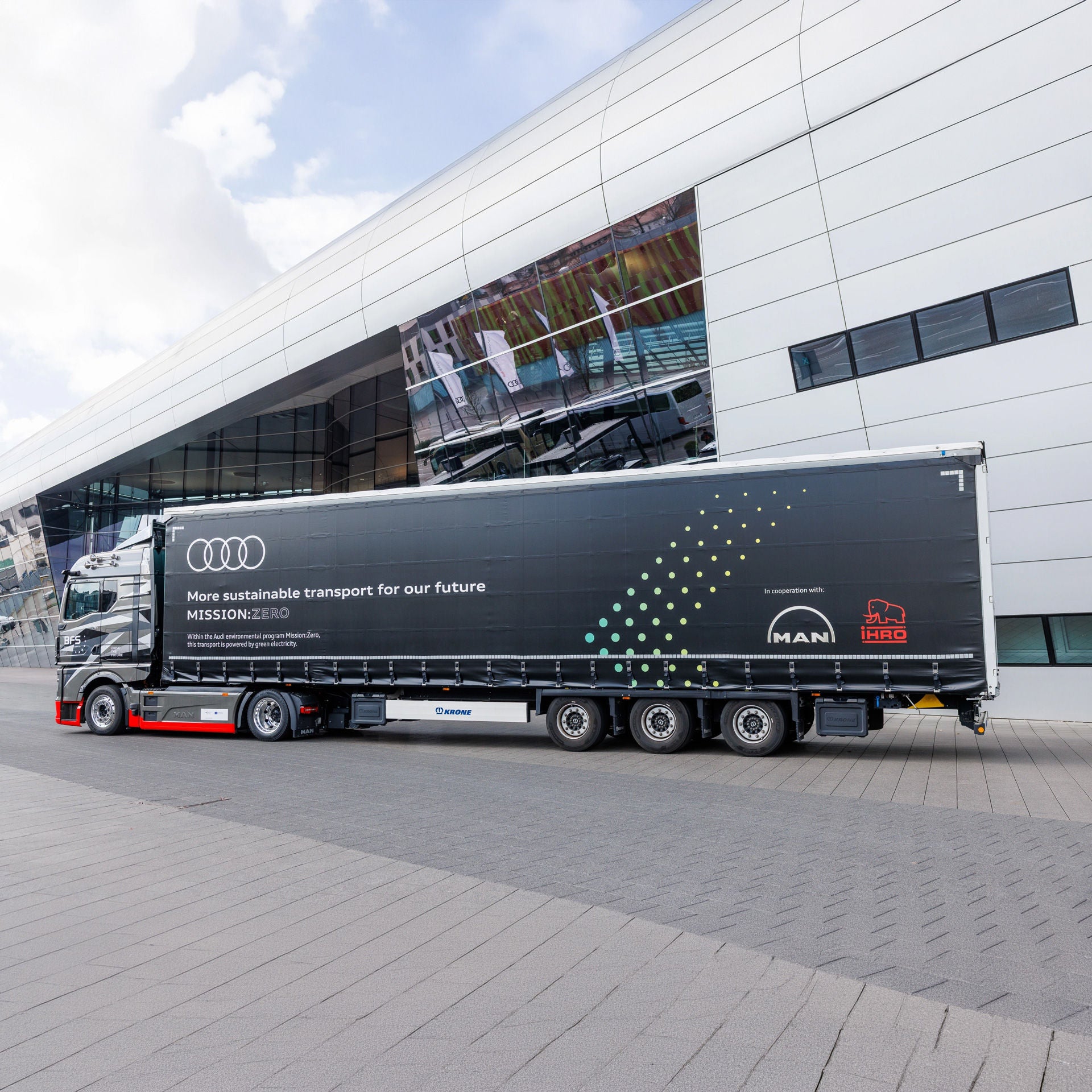 Electric truck with Audi branding in front of a modern building complex during a transport operation.