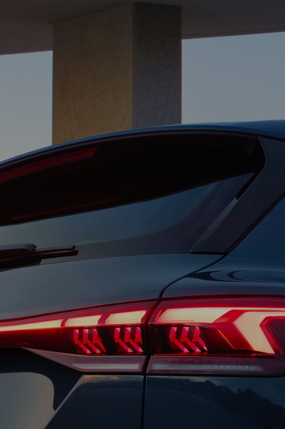 Close-up of an Audi vehicle's rear end showcasing sleek taillights and the iconic logo against a soft twilight background.