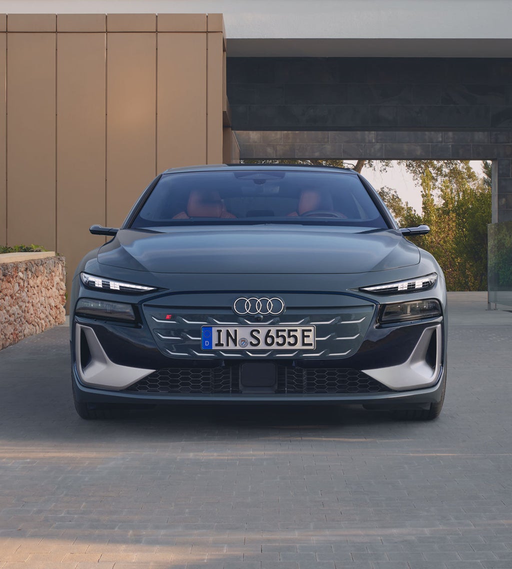 Frontprofil des S6 Avant e-tron, welcher auf Pflastersteinen vor einem modernen Gebäude steht.