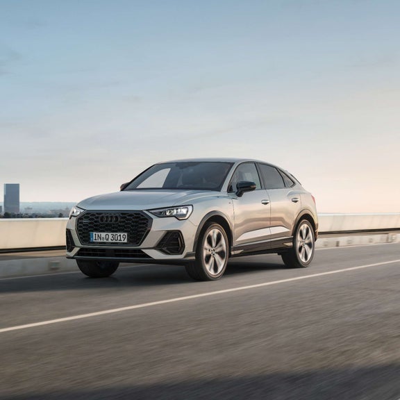 Silver Audi Q3 driving along a bridge with water and office buildings in the background