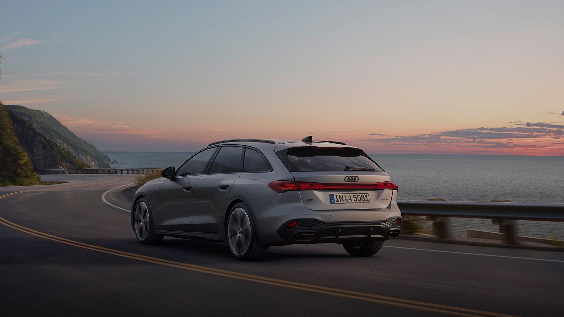 A silver Audi driving on a coastal road at dusk.
