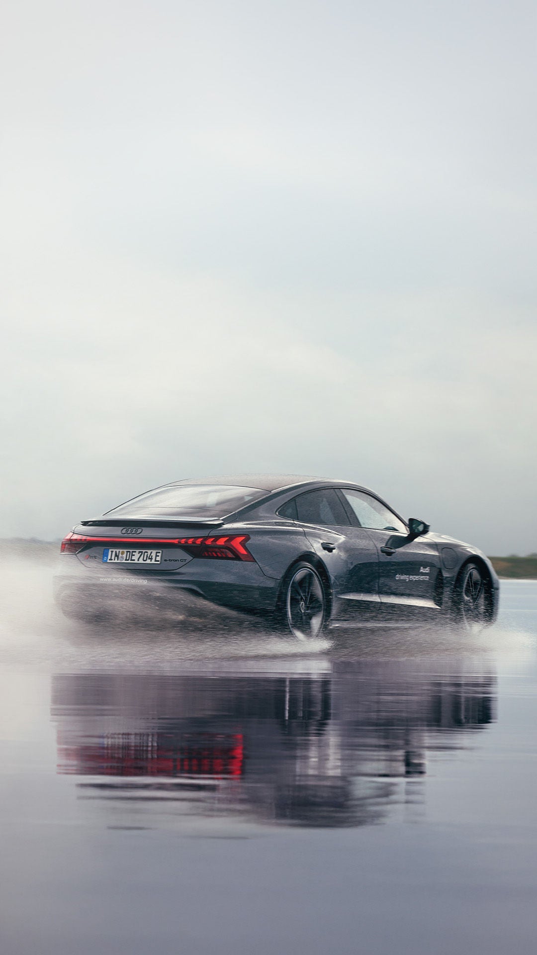Ein grauer Audi RS e-tron GT driftet auf einer nassen Teststrecke und wirbelt dabei Spritzwasser auf.