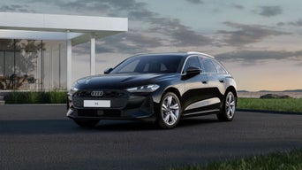 Une A5 Avant noire est garée devant une maison moderne aux murs vitrés, à la lisière de la nature.