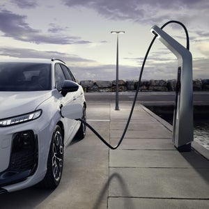 Ein weisser Q3 SUV e-hybrid an einer Ladesäule auf einem leeren Parkplatz.