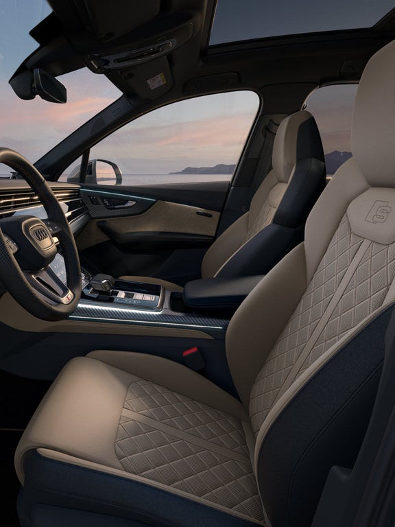 Innenraum eines Audi SQ7 SUV mit beigem Sportsitz, Multifunktionslenkrad und digitalem Cockpit mit Navigation bei Sonnenuntergang.