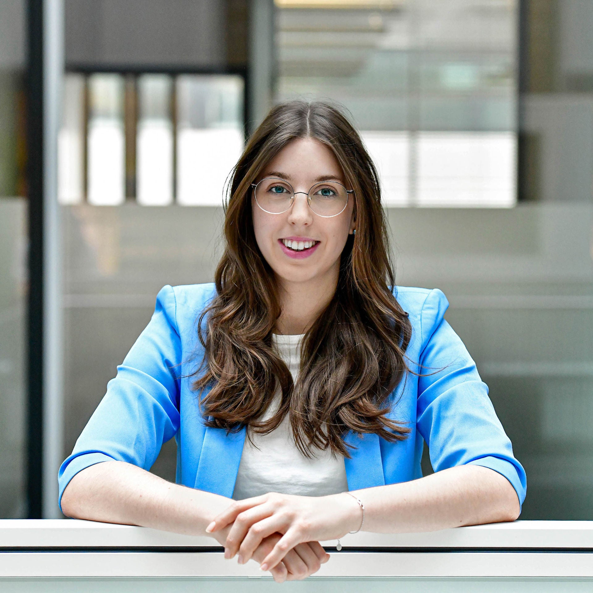 Woman with glasses and blue blazer smiles into the camera.