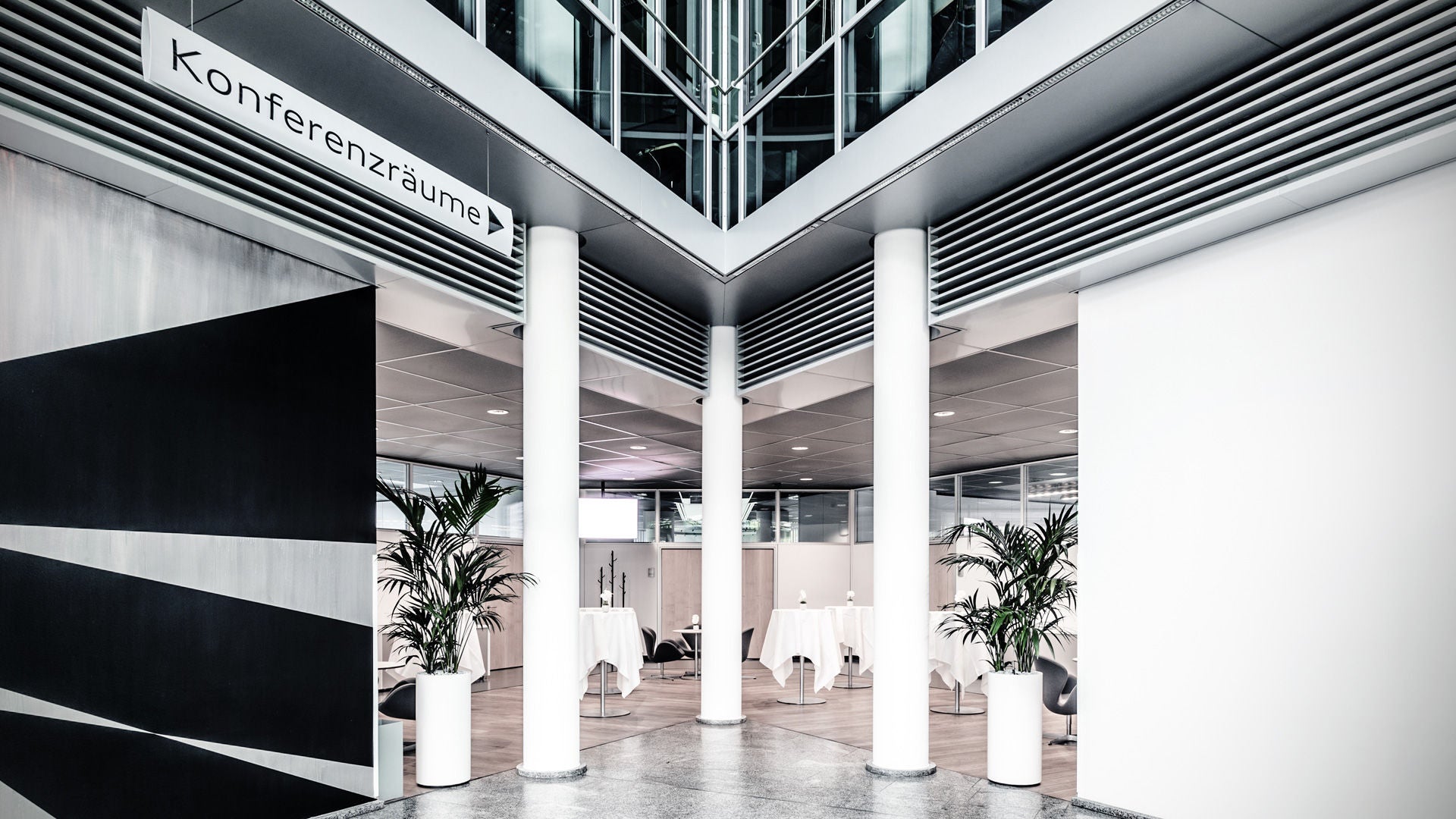 Eingangsbereich mit Schild „Konferenzräume“, weißen Säulen und Stehtischen mit weißen Tischdecken.