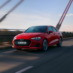 A red Audi A3 Saloon drives dynamically on a bridge against a clear blue sky.