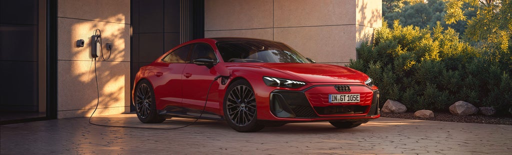Side view of a red Audi e-tron Gt parked in front of a modern house. with an electric charged mounted on the wall