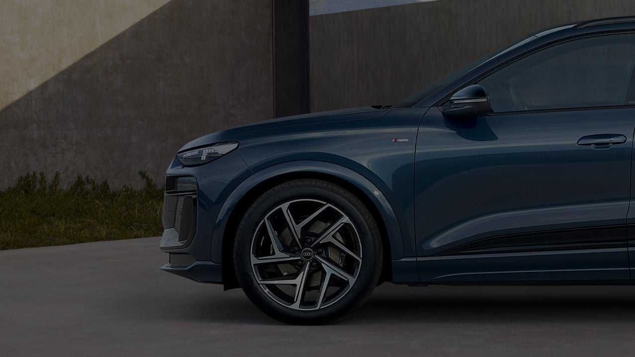Side view of a blue car with stylish alloy wheels, set against a modern concrete backdrop and green grass.