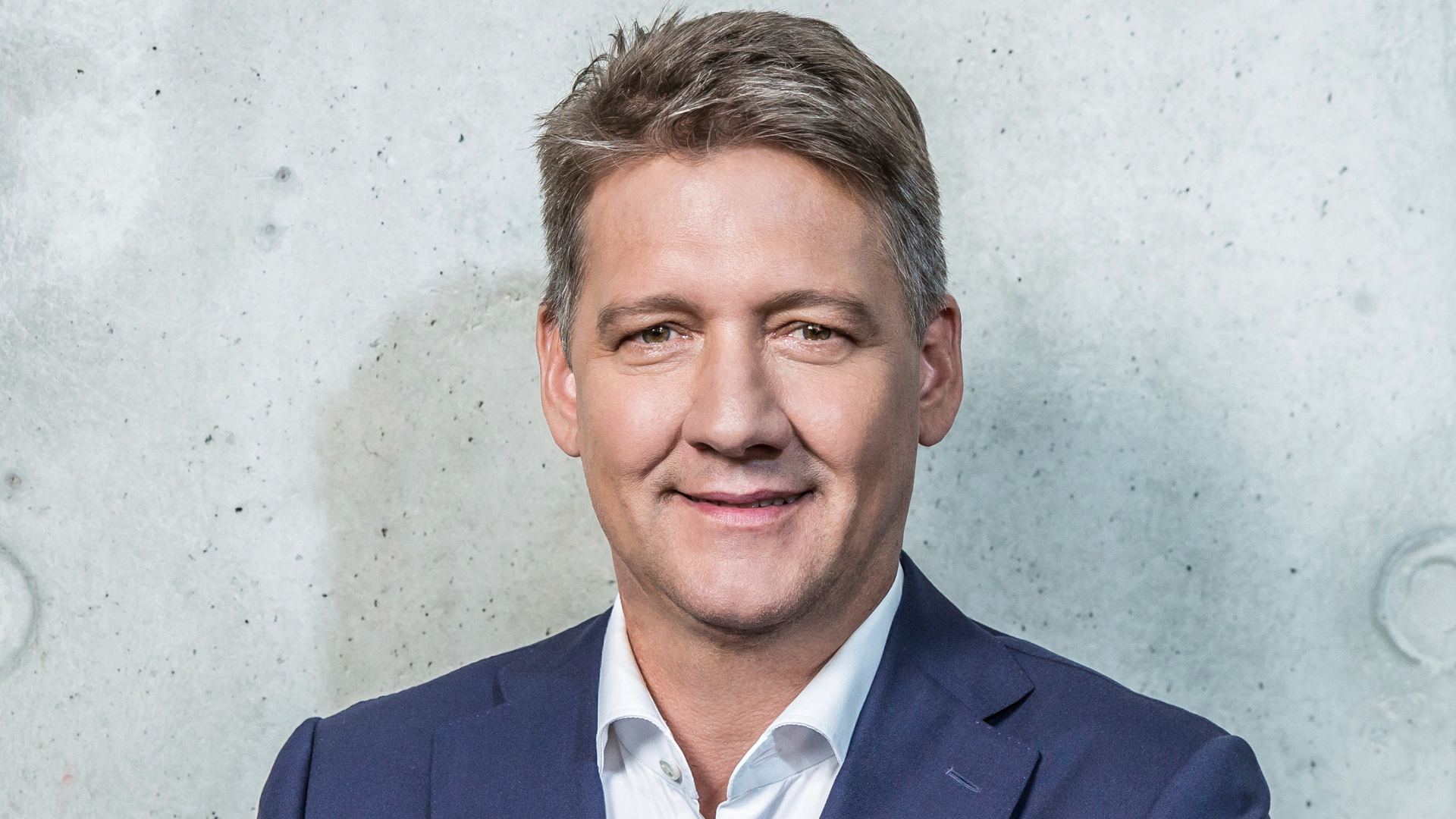 Portraitbild von CEO Gernot Döllner vor einer hellen Steinwand.