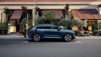 Une Audi Q4 e-tron bleue garée dans une rue bordée de magasins dotés de terrasses et de plantes.
