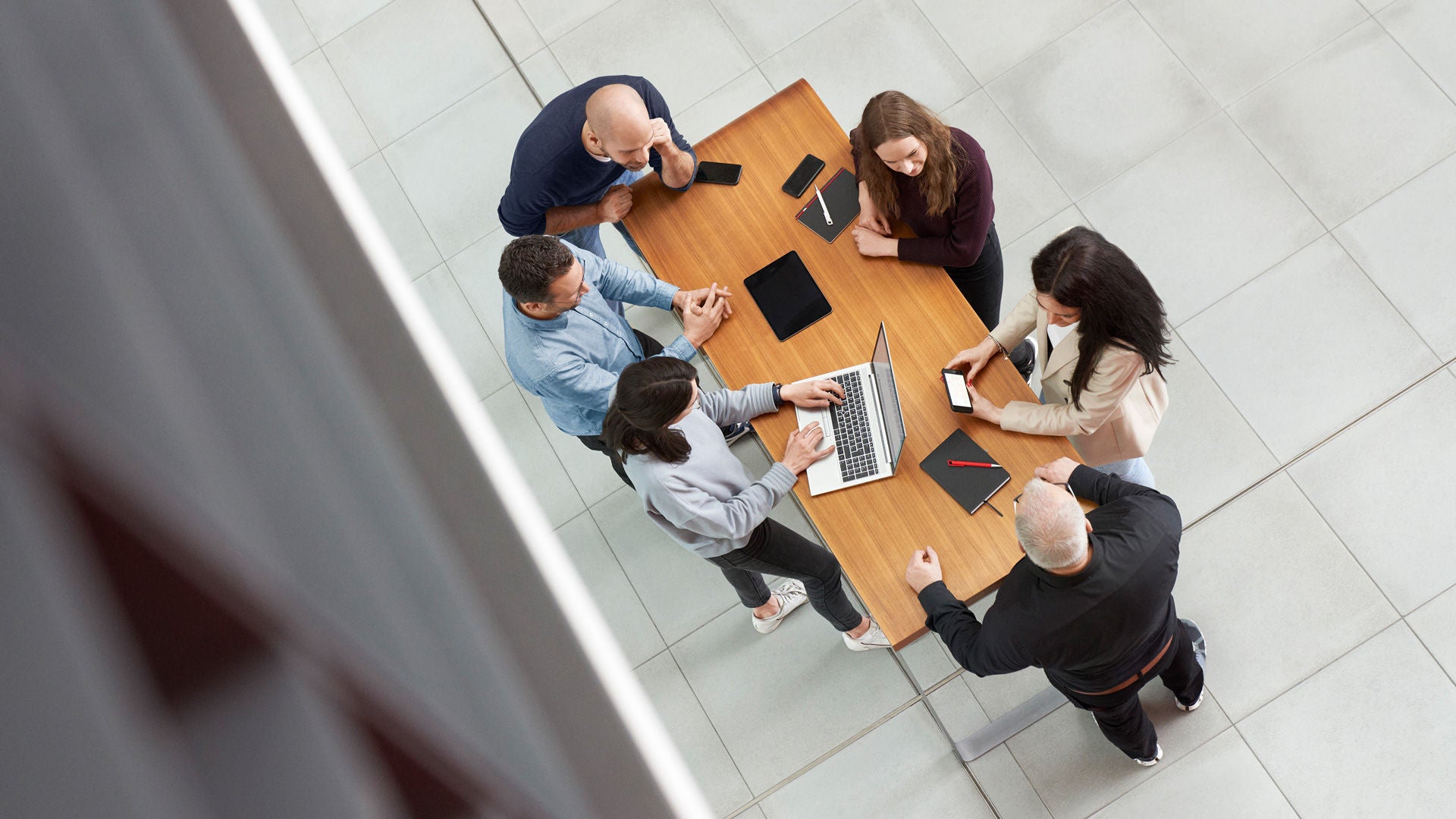 View from above: six people are standing at a table with laptops and talking together.