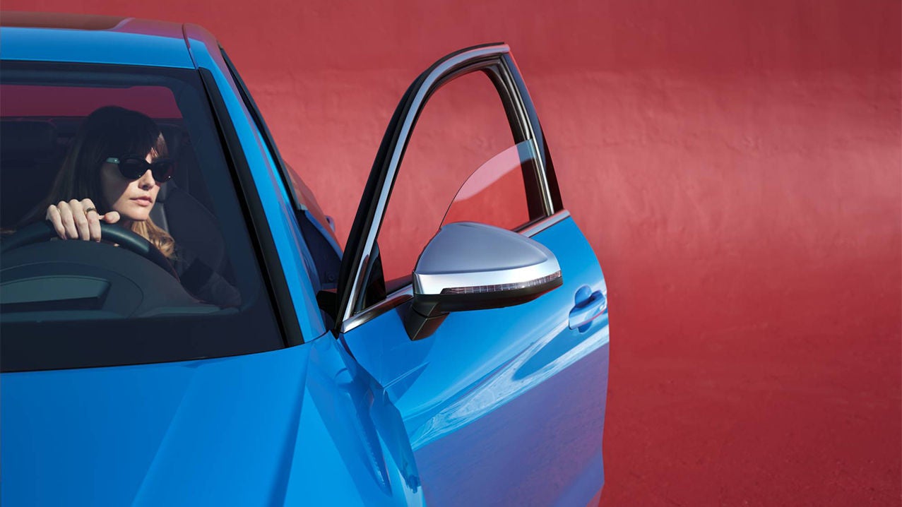 Persona con gli occhiali da sole in un’Audi blu davanti a una parete rossa