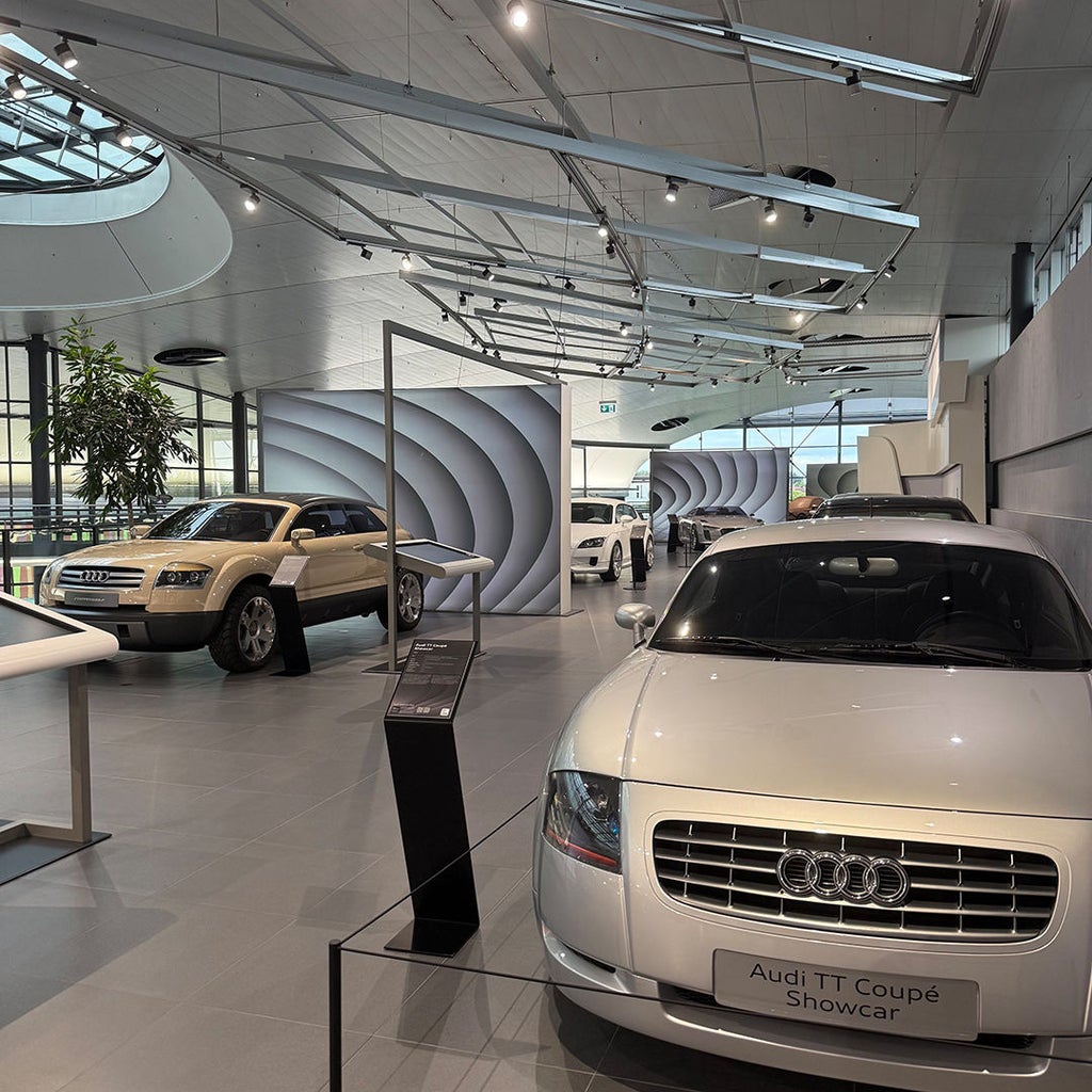 Audi TT Coupé Showcar in Silber im Vordergrund einer modernen Ausstellungshalle mit weiteren Audi-Fahrzeugen.