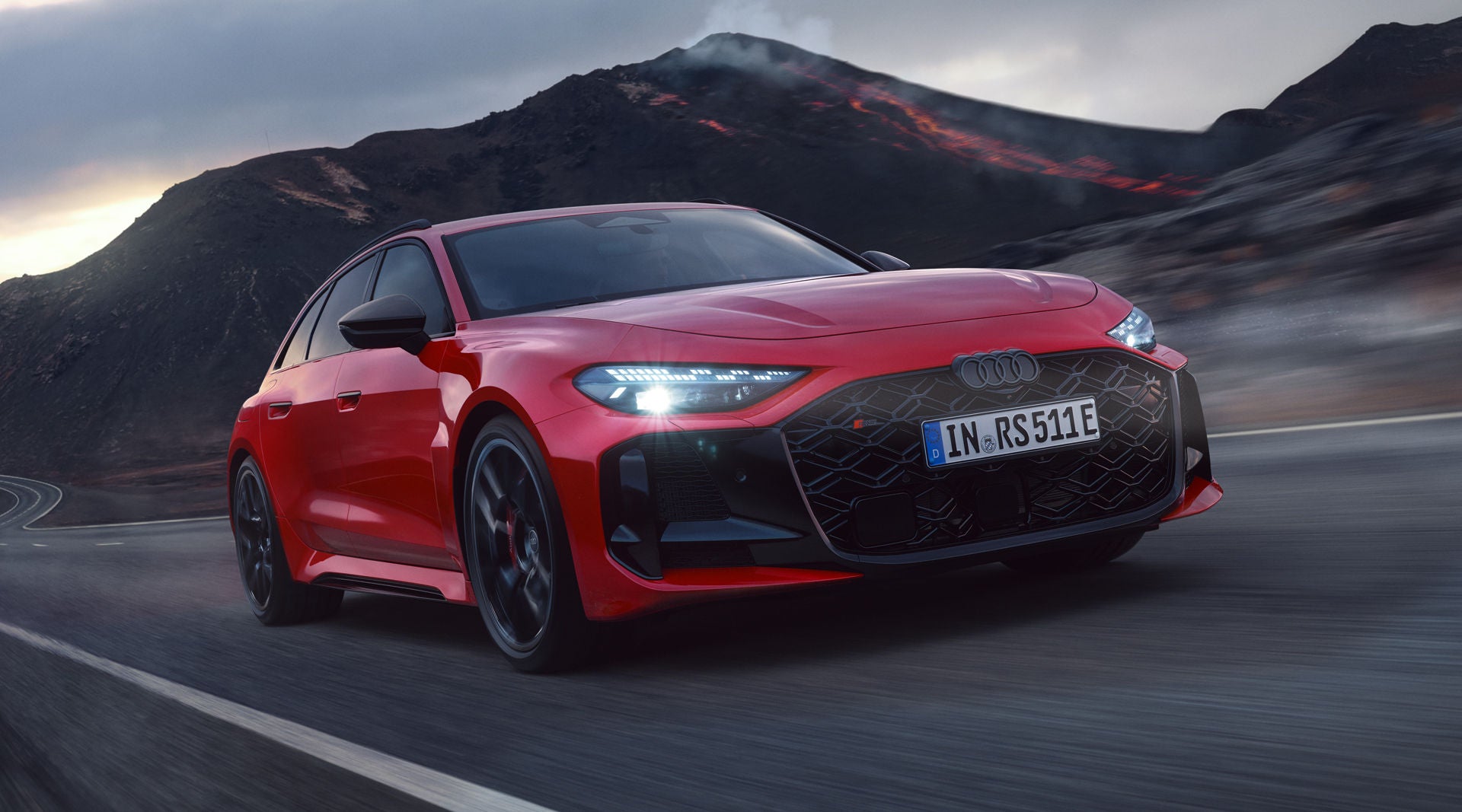 The RS 5 Avant is seen from a diagonal front angle driving on a mountain road in a volcanic landscape.