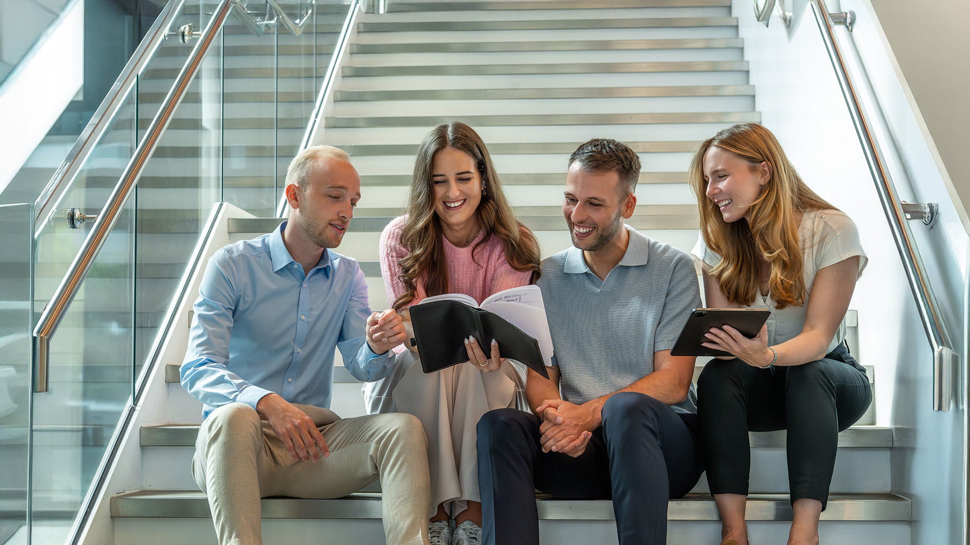 Graduates sit on stairs and look at a book held by a female graduate