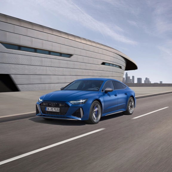 Blue sedan driving on road with modern building and city skyline in the background.