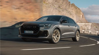 A silver Audi RS Q8 SUV driving along a coastal road with motion blur