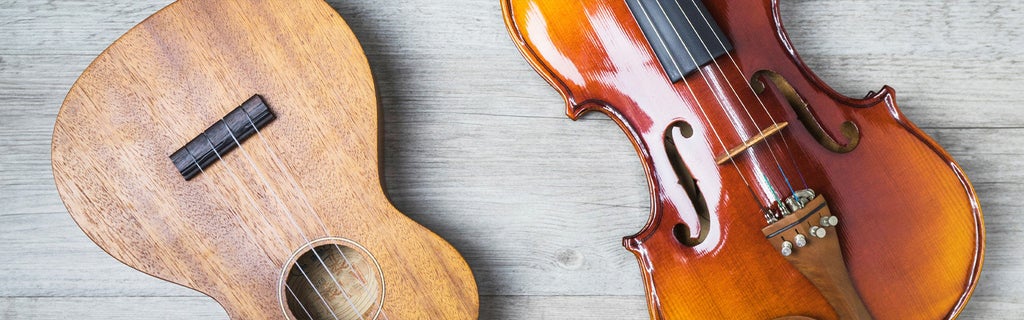 Gitarre und Violine liegen nebeneinander auf einem hellen Holzboden.